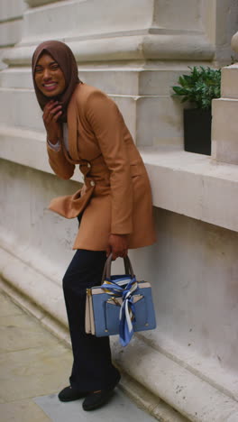 vertical video portrait of smiling muslim businesswoman wearing hijab and modern business suit standing outside city office buildings 9