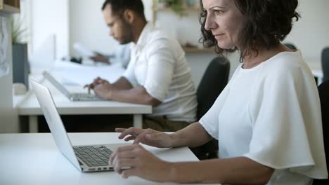 vista lateral de una mujer caucásica enfocada trabajando con una computadora portátil