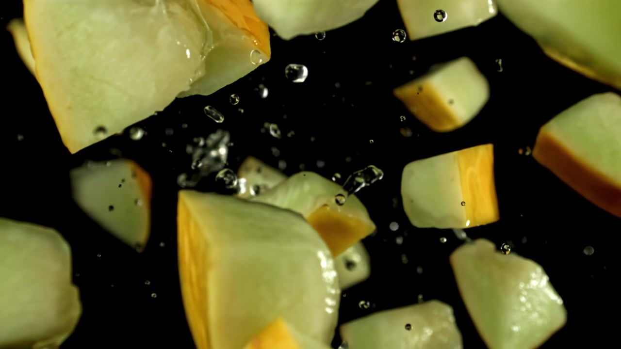 Diced Melon Pieces Falling with Water Droplets in Slow Motion