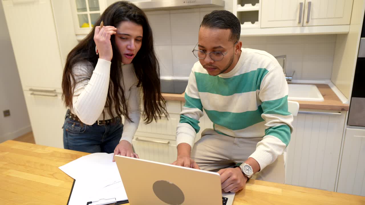 Multiethnic Couple Working on Laptop and Documents in Kitchen