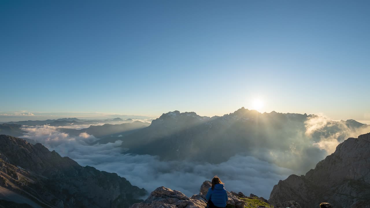 Un escursionista osserva un tramonto maestoso con nuvole basse al Rifugio di Collado Jermoso nei Picos de Europa, León, Spagna.