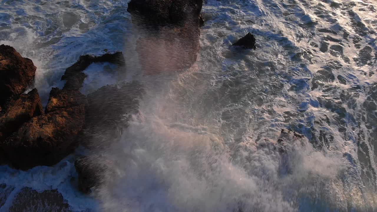 las olas del océano bañan los acantilados a la hora dorada, vistas directamente desde arriba