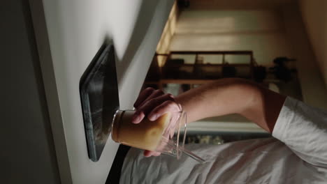 hombre de video vertical agarrando un café con leche helado en una taza de vidrio con pajita de vidrio del mostrador de la cocina en casa en cámara lenta