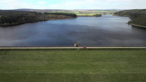 aerial flyover from swinsty to fewston reservoir with car crossing dam inbetween