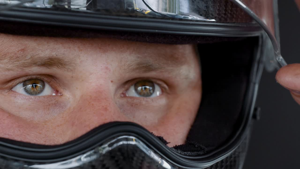 Racing driver stares with serious eyes while he shuts his helmet visor in slow motion.