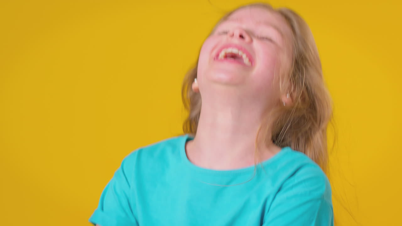 Ritratto in studio di ragazza con capelli lunghi che ride, su sfondo giallo.