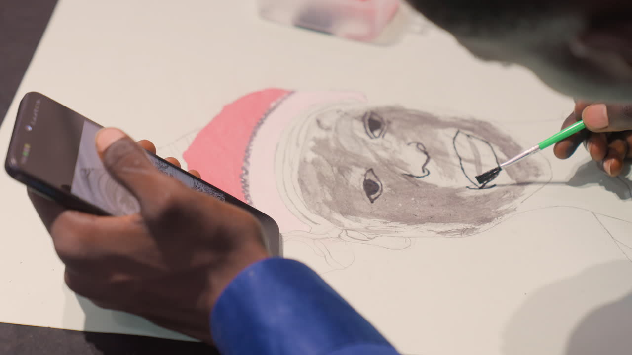 Artista negro pintando um retrato com pincel usando o telefone como referência, adicionando sombreamento fino à boca e aos olhos, energia de demonstração ao vivo, configuração de mesa de estúdio, detalhe de boné rosa, ritmo de tutorial, movimentos de mão focados.