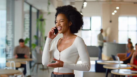 smiling businesswoman standing in busy open plan office talking on mobile phone