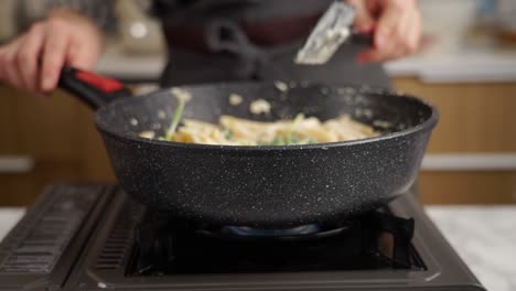 anonymous cook stirring pasta in frying pan with spatula