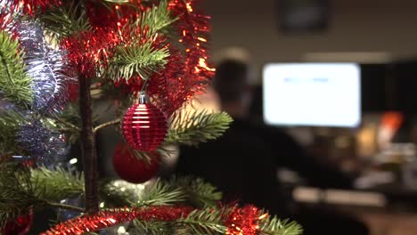 Christmas-decoration-in-an-office,-while-man-working-overtime-in-the-background