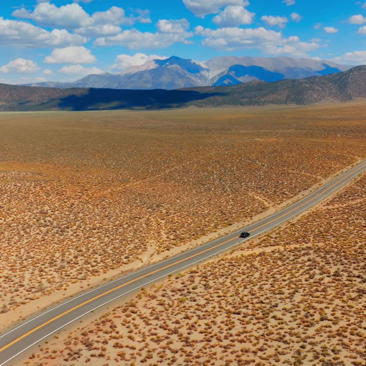 Lonely black car on the road to Nevada, USA. Beautiful sight of desert contrasting with blue skies. Mountains at backdrop