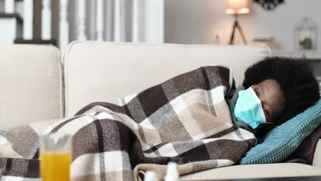 close up of african american female wearing a medical mask and lying on sofa