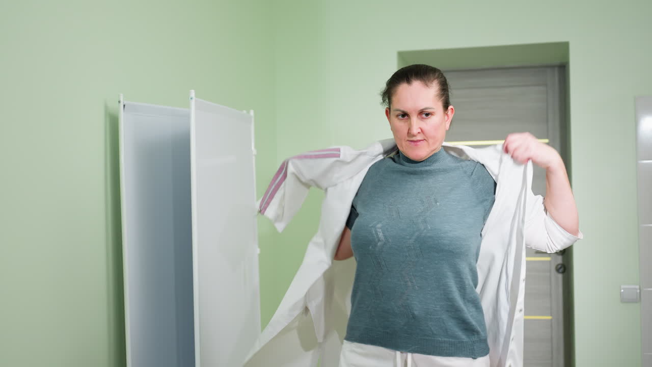 Therapist confidently wears uniform while scanning room with attentive gaze inside clean medical facility, preparing for workday responsibilities in clinical setting under bright lighting