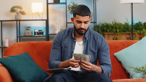 Rich-happy-Indian-man-using-calculator-counting-money-cash-salary-calculate-domestic-bills-at-home