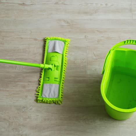 cleaning the house. green bucket and mop on the parquet floor. microfiber brush is mopping the floor. householding tools. top view.