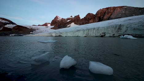 una escena mañanera pacífica en el lago glacial junto al glaciar claridenfirn en uri, suiza, con los picos alpinos detrás de la pared de hielo y los icebergs flotando en primer plano.