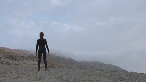 tiro largo de una mujer por detrás con ropa negra en un desierto al amanecer