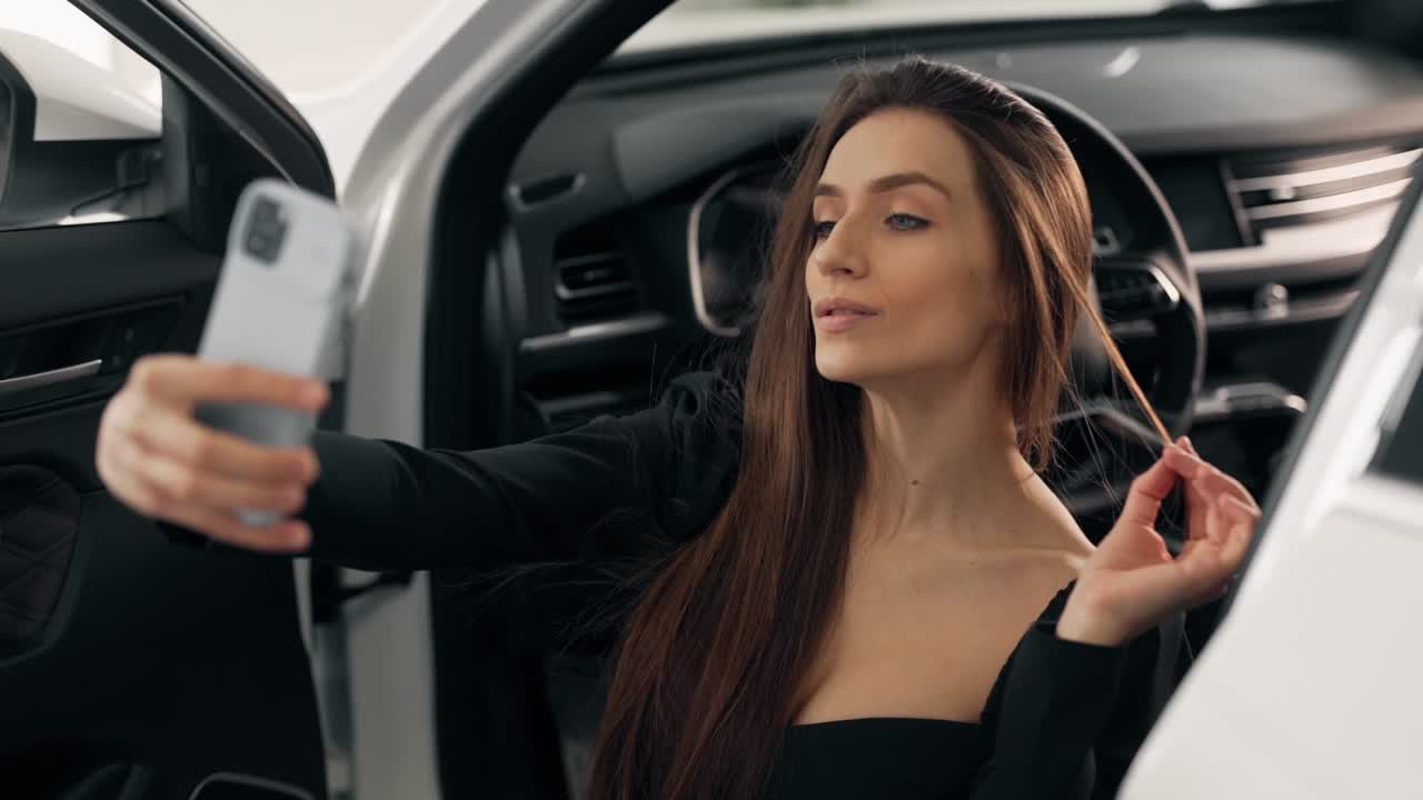 hermosa chica en un traje sexy hace un selfie sentado en un coche nuevo