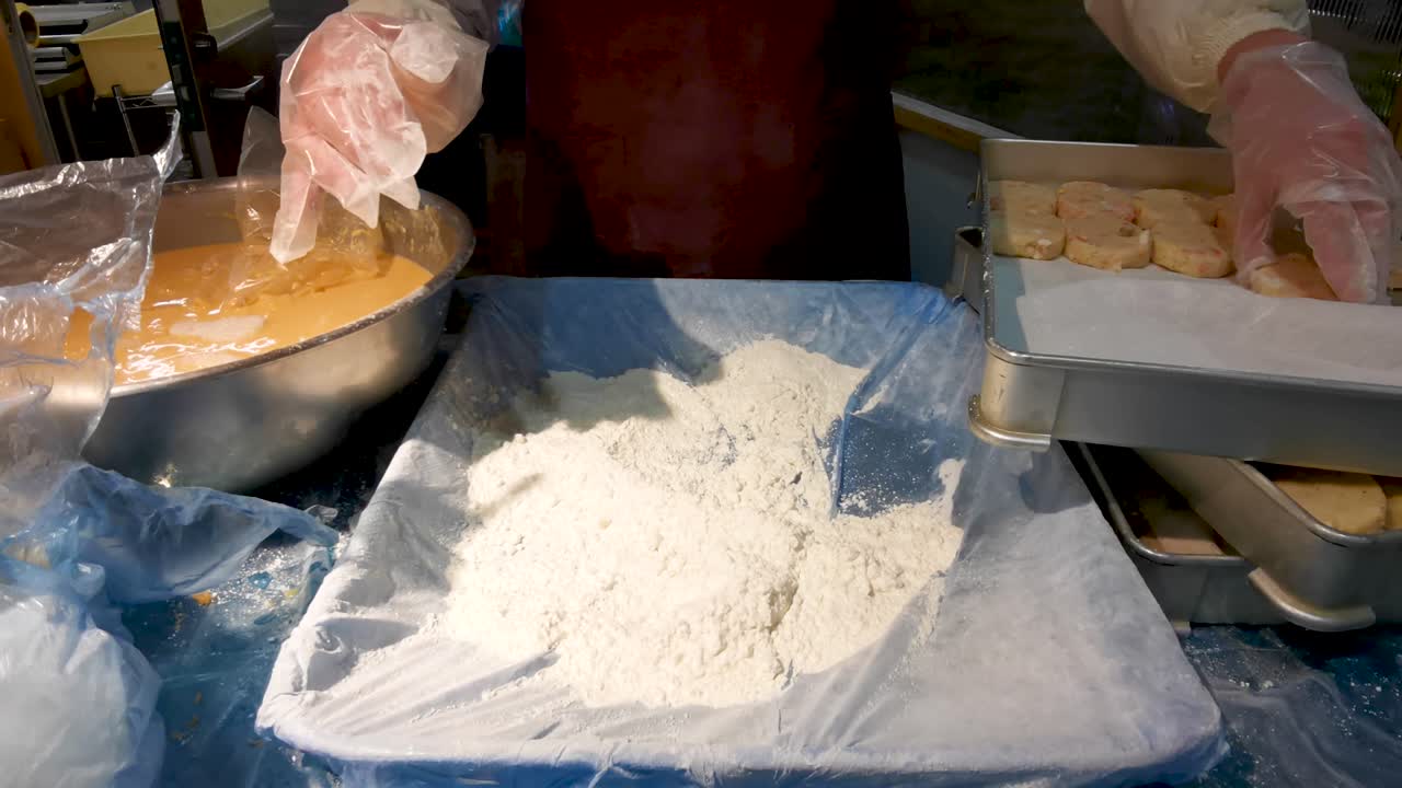 Close-up view of a person preparing food, breading and frying