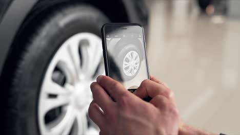 close-up of male hands taking pictures with smartphone of new wheel in car