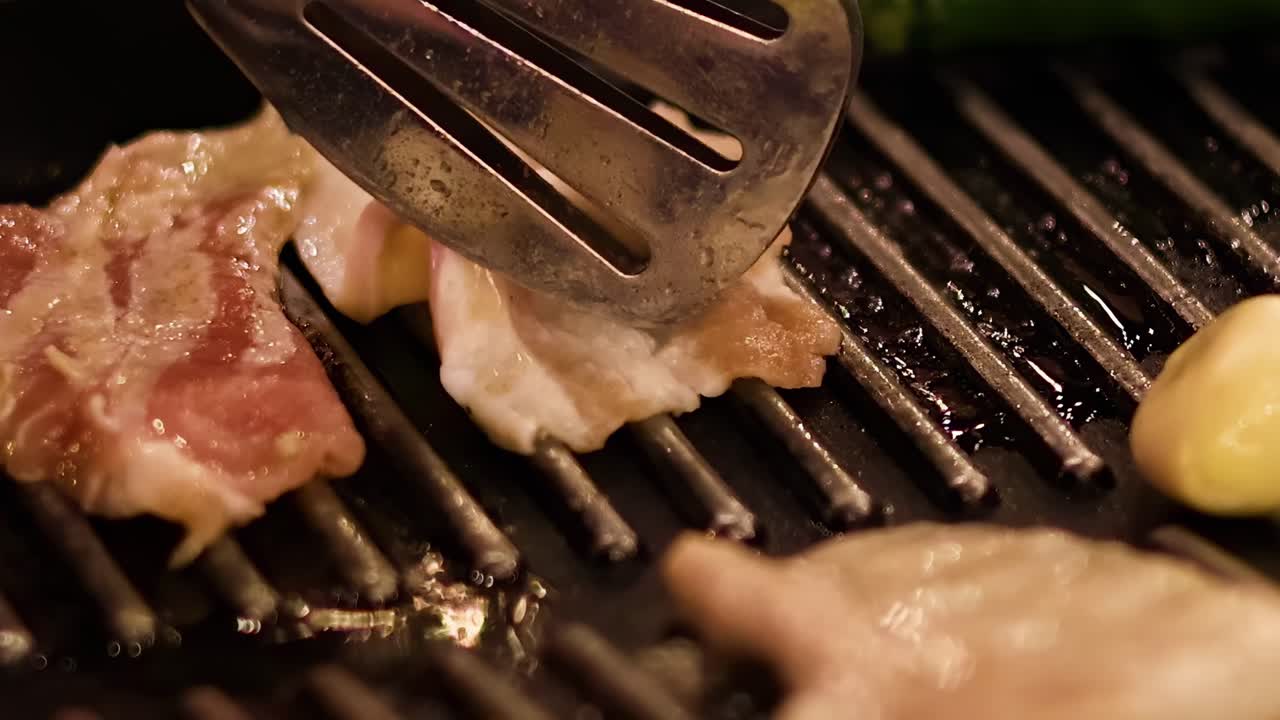 Close-up of pork slices being grilled with tongs, showcasing grill marks and sizzling heat.