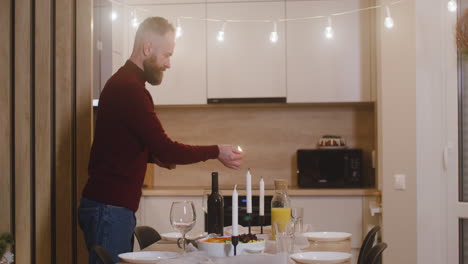 red haired man lighting a candle that decorates the christmas table setting