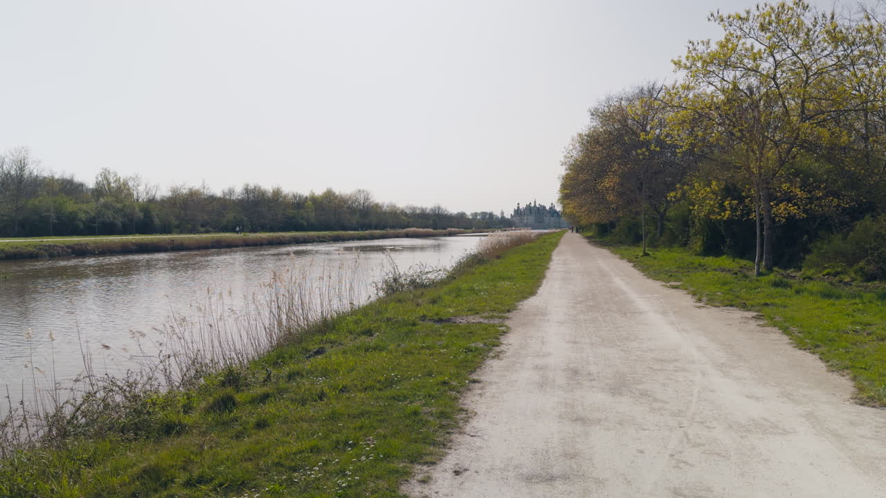 Peaceful canal path leading to Château de Chambord, springtime with trees and tourists