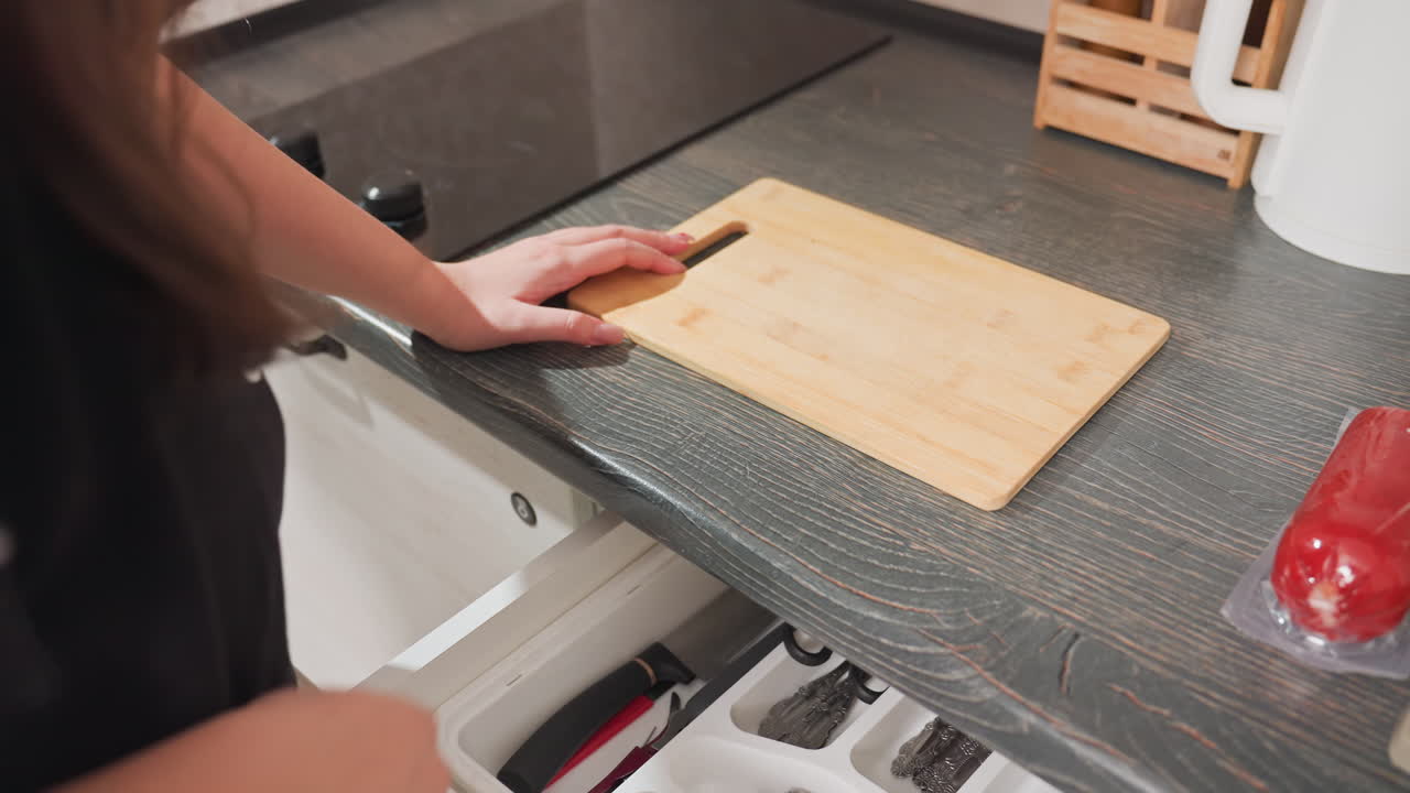close up rear view woman closing first drawer and returning cutting board into second drawer kitchen preparation cooking scene with hotdog on countertop domestic lifestyle modern kitchen interior