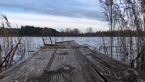 Antigua-Pasarela-De-Madera-En-El-Lago,-Contra-El-Fondo-Del-Cielo-Azul-Y-Magníficos-Verdes-Alrededor