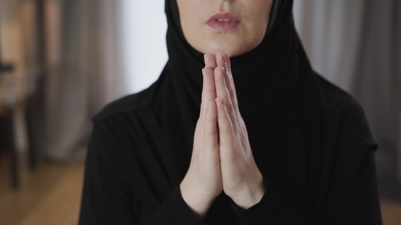 Close-up of female hands folded together. Unrecognizable young Muslim woman praying at home. Religion, lifestyle, culture.