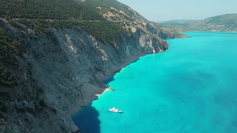 Luxury-yacht-on-turquoise-water-by-rocky-cliffs-in-the-Kefalonia-Island,-Aerial-dolly-shot