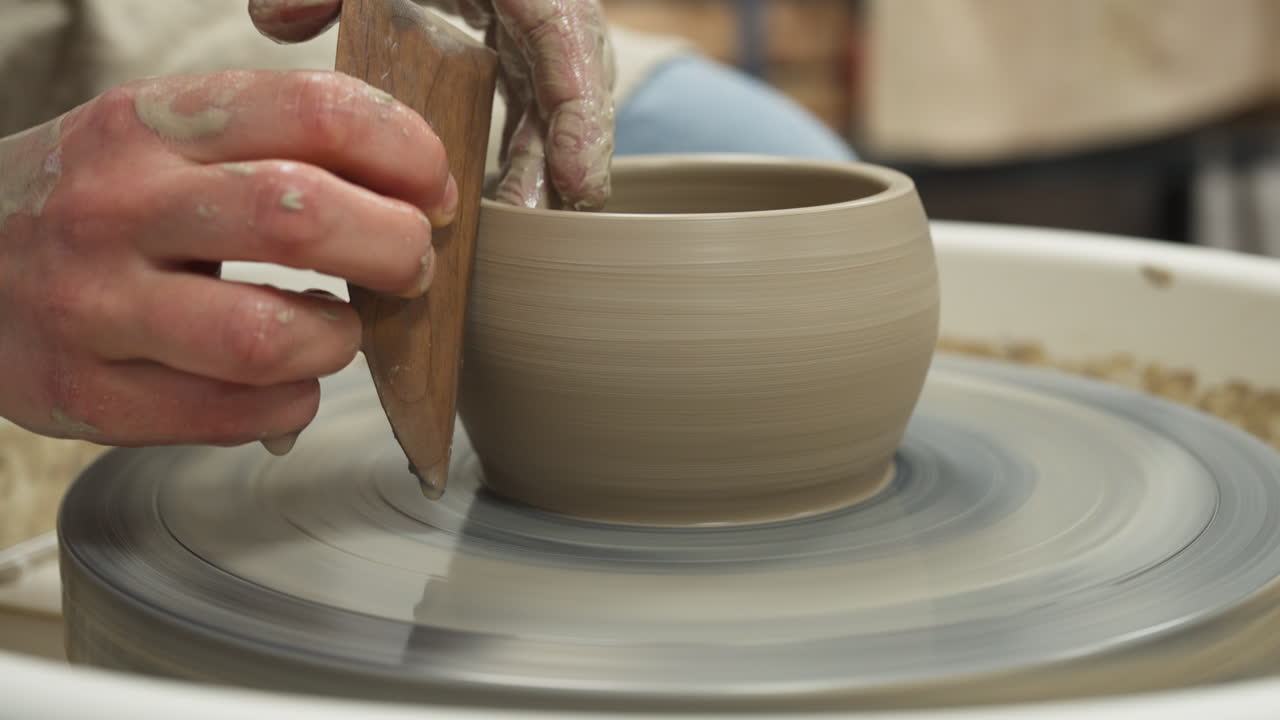Close up shot of white hands making mug from clay with a piece of wood, interior