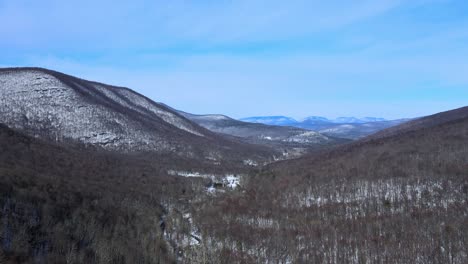 aerial drone footage of a snowy mountain valley in early spring on a sunny day in the appalachian mountain range, just after winter ends with forests and snow and sunshine and blue skies