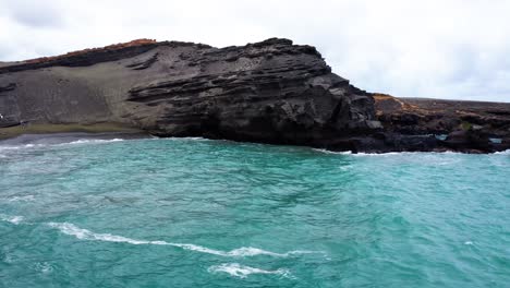 vivid turquoise sea gently laps against rugged volcanic cliffs and a black sand shoreline, showcasing the raw beauty of this unique coastal landscape.
