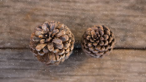 nieve cayendo sobre dos conos de pino en la superficie de madera