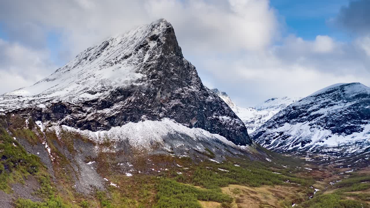 A lonely mount Hereggja soaring above the lush Herdalen valley. Farmland stretching up to the foothills of the mountain range. Waterfalls cut the mountainsides. White clouds rushing above.