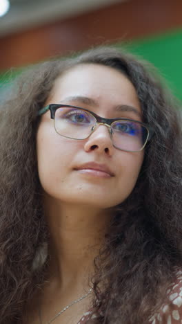 mujer curiosa con gafas de pie en un centro comercial ocupado, mirando a su alrededor con interés, las características de fondo muestran tiendas, iluminación suave, y la gente caminando por
