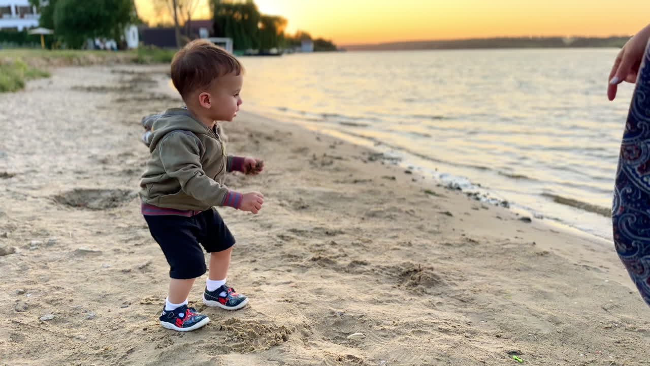 Lovely Caucasian toddler having good time at the sea shore. Baby boy picks some sand from the beach.