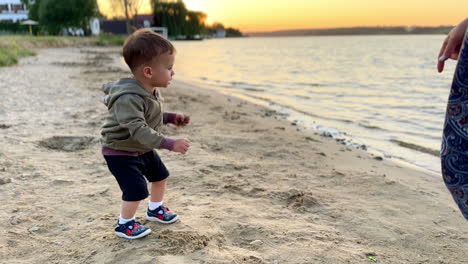 lovely caucasian toddler having good time at the sea shore. baby boy picks some sand from the beach.