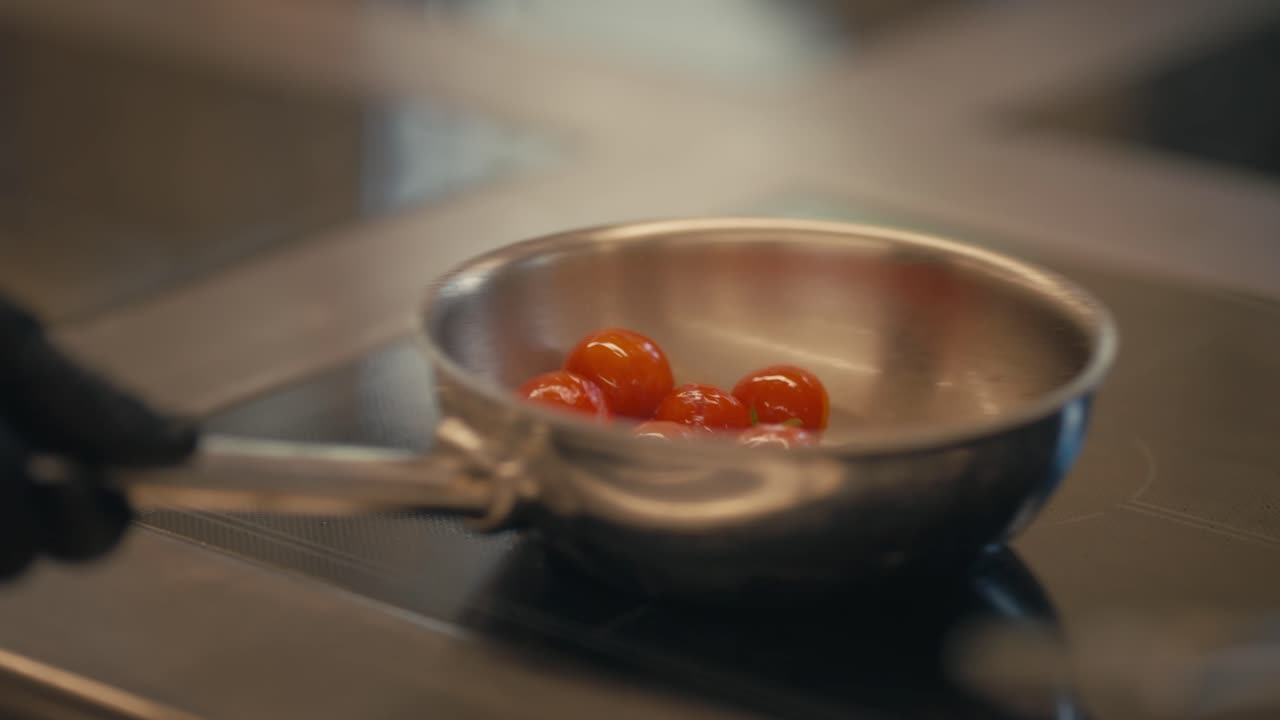 Chef cooks cherry tomatoes in steel pan, close up