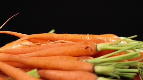 a fresh baby carrot falls onto a pile of carrots against a black background, captured in slow motion with bright, even studio lighting and shallow depth of field
