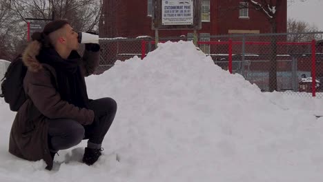 jovem ajoelhado no parque nevado em rosemont borough de montreal toma café quente ou chocolate quente