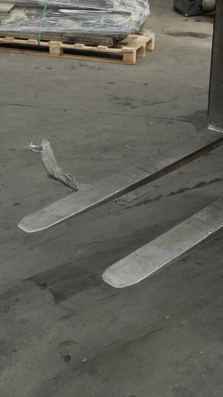 Tomme gaffeltruckgafler hviler på et betongulv på et lager nær en indpakket palle på en fabrik.