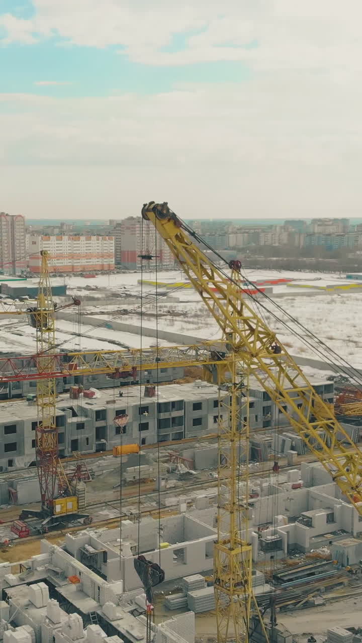 view of undone building project with large yellow construction cranes against snow field and residential area upper view