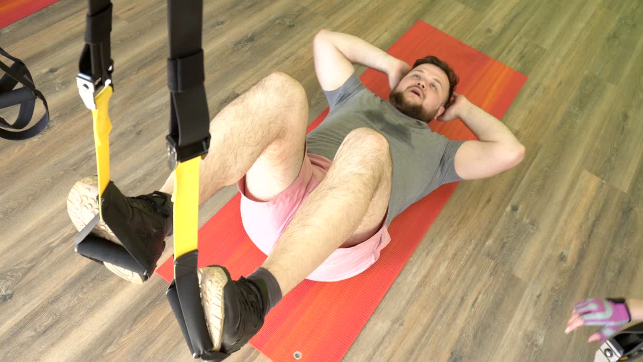 gordo hombre caucásico barbudo trabaja en un centro de fitness moderno en bucles de trx, desarrollando resistencia y músculo, exceso de peso