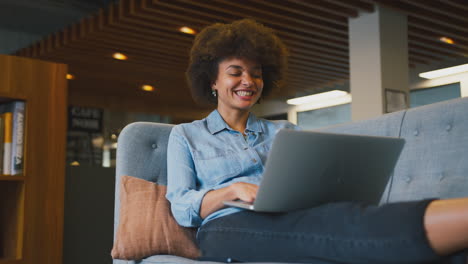 Young-Businesswoman-In-Modern-Open-Plan-Office-Working-On-Laptop-In-Casual-Seating-Area