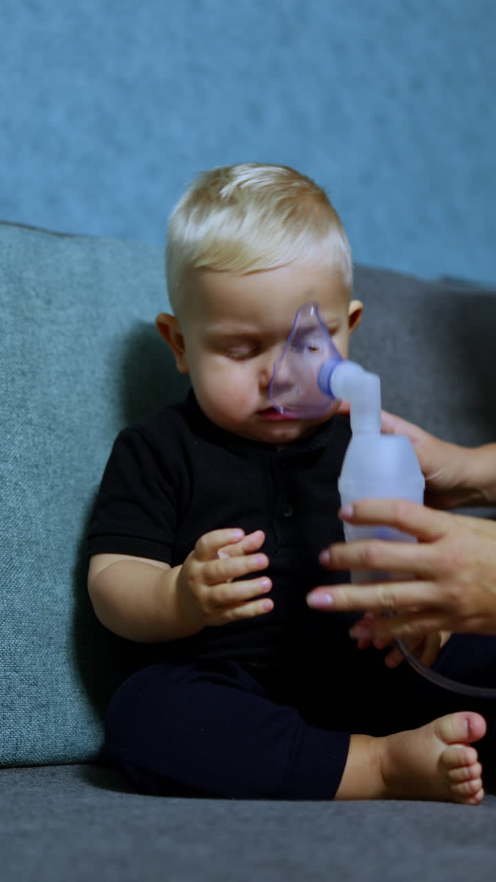 Un bambino piccolo è seduto sul divano e respira con un inalatore. Inalazione terapeutica per bambini. Maschera per inalazione per bambini