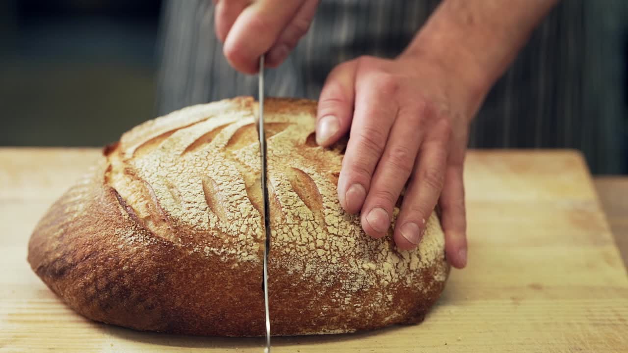 baker's hands are cutting home-made fresh wheat rye bread