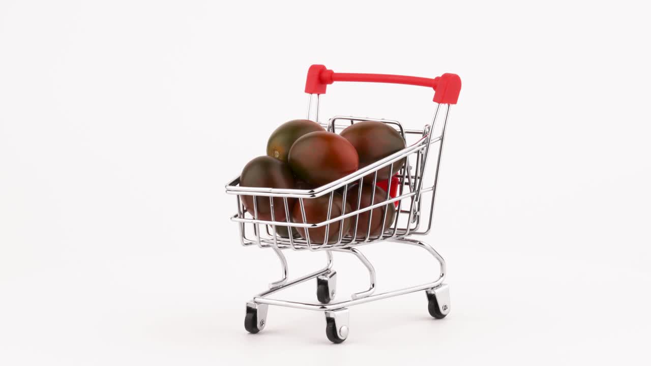 Nákupní vozík plný hromady černých cherry rajčat. Otáčí se na otočném talíři. Izolováno na bílém pozadí. Detailní záběr. Makro