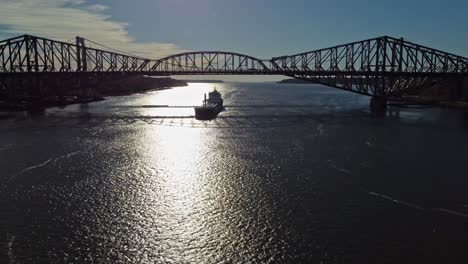 Disparo-De-Drones-Yendo-Hacia-Atrás-Mientras-Un-Barco-De-Carga-Viaja-Bajo-El-Puente-De-Quebec